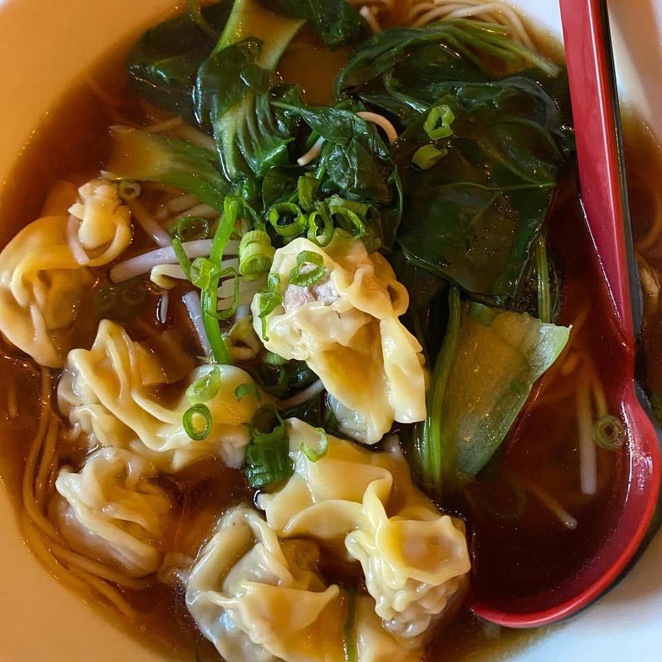 Close-up of Momo Ramen's wonton ramen with bok choy, bean sprouts, and scallions in a rich broth.