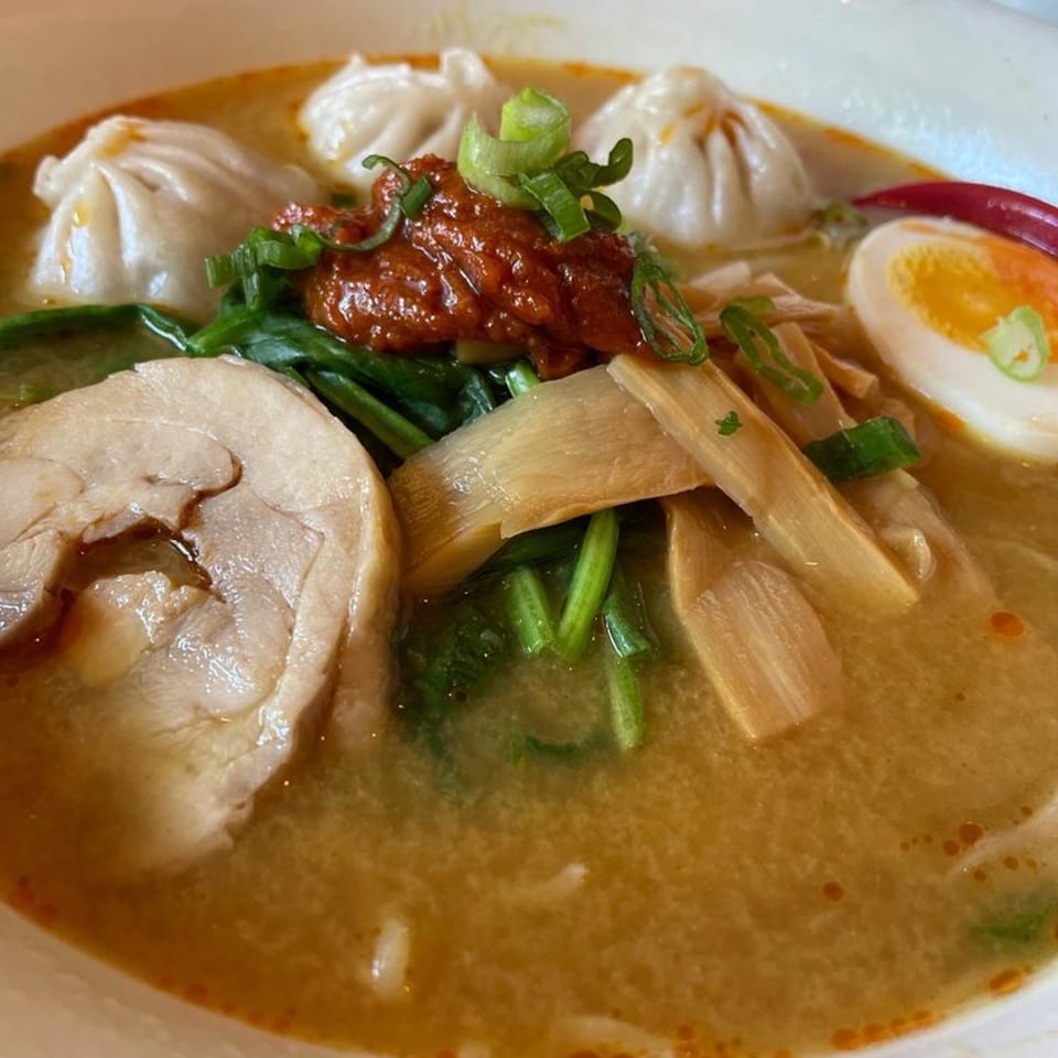 A close-up of Momo Ramen's ramen bowl, featuring chicken, dumplings, egg, bamboo shoots, and chili paste.